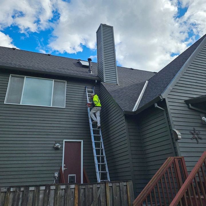After: the chimney chase with new siding, a roofer on the ladder beside it