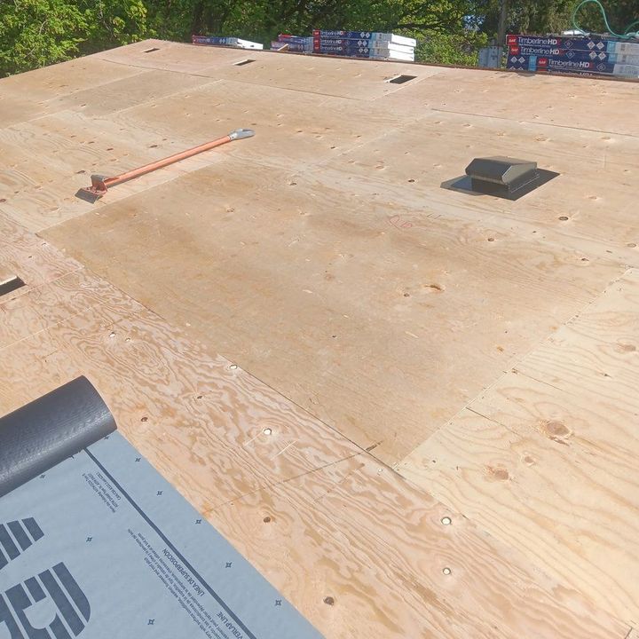Before: bare plywood decking with a new vent set, GAF Timberline shingle bundles staged along the ridge and underlayment rolling out